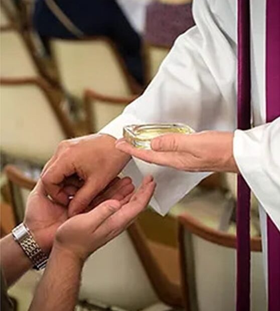 A priest anoints a person’s hands with the Oil of the Sick