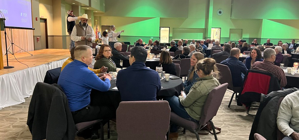 Fundraising event with people seated around table and auction happening on a stage